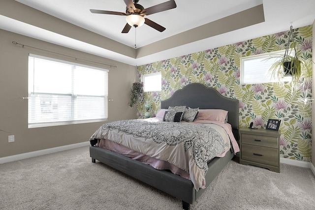 carpeted bedroom featuring wallpapered walls, a tray ceiling, and baseboards