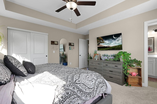 bedroom featuring carpet, a closet, ensuite bath, a raised ceiling, and a ceiling fan