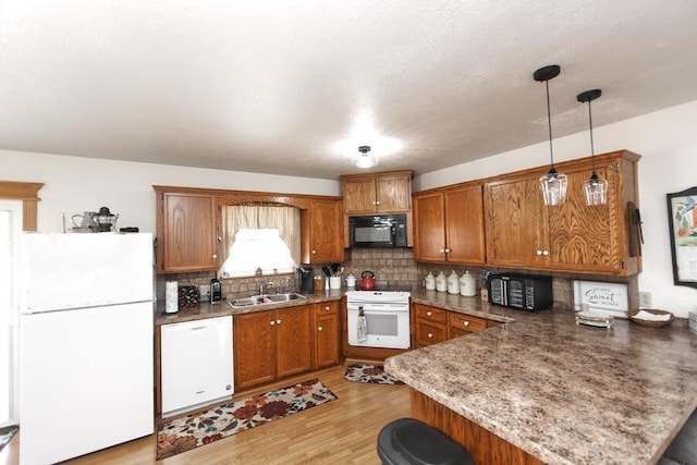 kitchen with brown cabinets, white appliances, a peninsula, and a sink