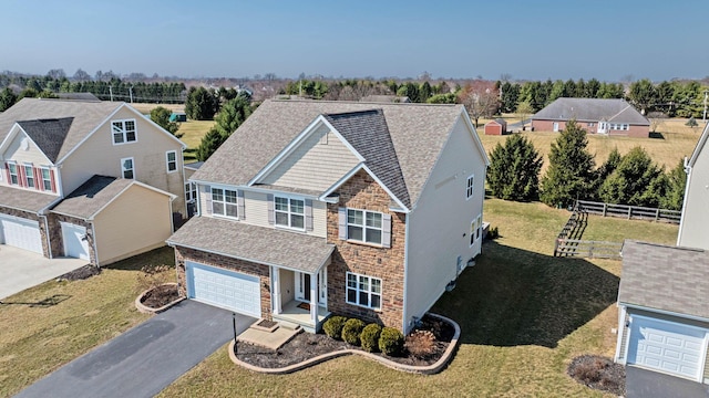 traditional-style home featuring a shingled roof, a front lawn, fence, aphalt driveway, and stone siding