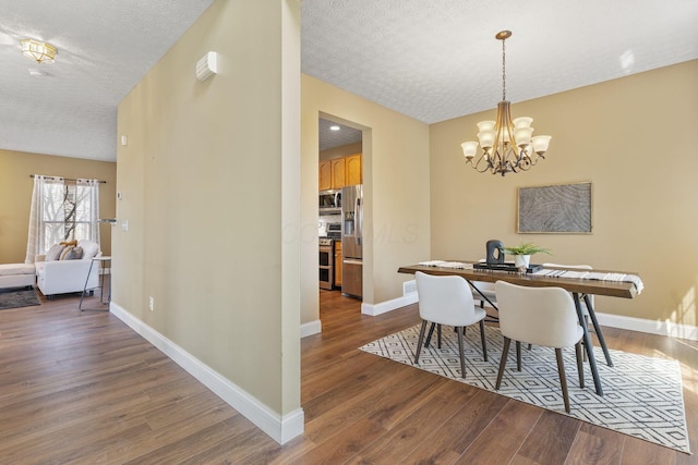 dining space featuring a chandelier, a textured ceiling, baseboards, and wood finished floors