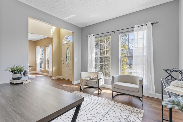 foyer entrance with baseboards, a textured ceiling, and wood finished floors