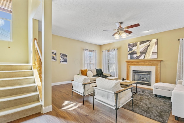 living room featuring a high end fireplace, ceiling fan, stairway, wood finished floors, and a textured ceiling