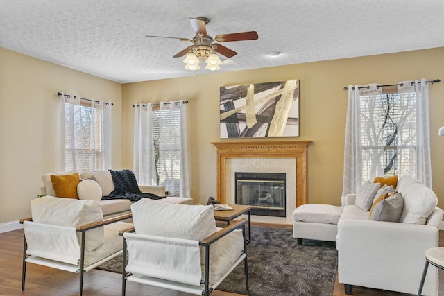 living area with baseboards, a premium fireplace, wood finished floors, a textured ceiling, and a ceiling fan