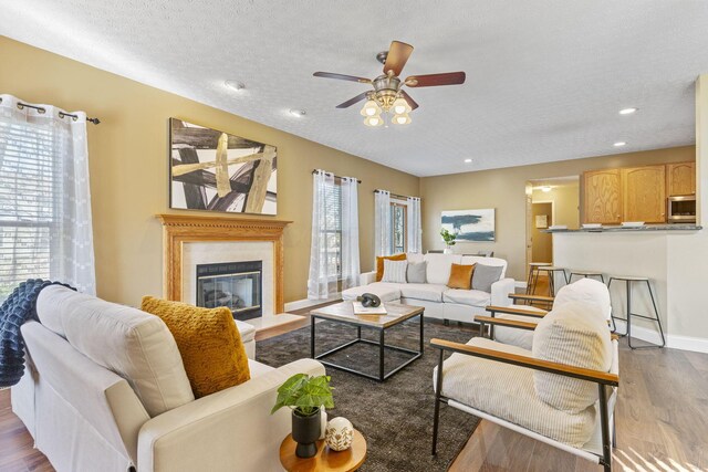 living area featuring a textured ceiling, a glass covered fireplace, wood finished floors, baseboards, and ceiling fan