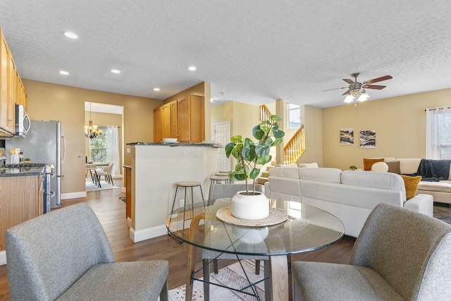 dining room featuring dark wood-style floors, ceiling fan with notable chandelier, stairs, and a wealth of natural light