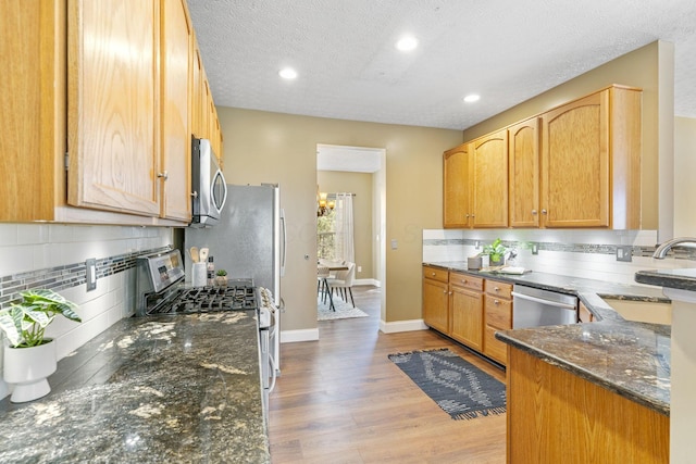 kitchen featuring baseboards, dark stone counters, light wood-style flooring, stainless steel appliances, and a sink