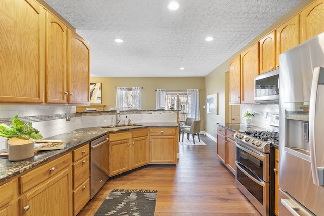 kitchen featuring a peninsula, dark wood-style flooring, a sink, decorative backsplash, and appliances with stainless steel finishes