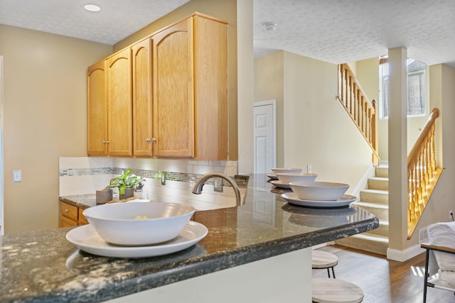 kitchen featuring a kitchen bar, dark stone countertops, backsplash, a textured ceiling, and wood finished floors