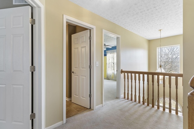 hallway featuring baseboards, carpet floors, a textured ceiling, and an upstairs landing