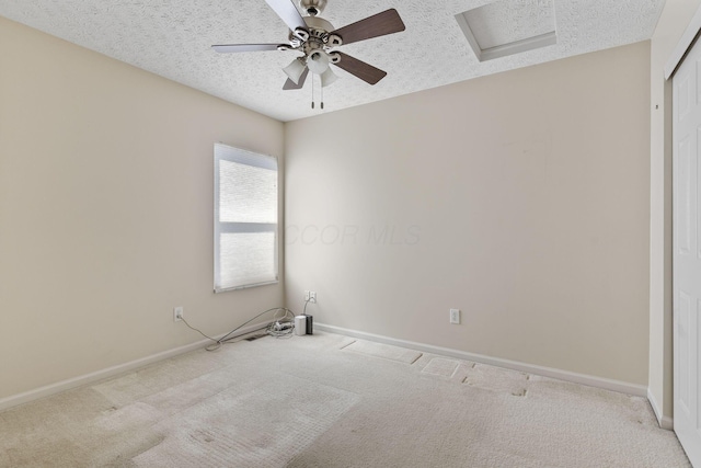 empty room featuring ceiling fan, attic access, carpet flooring, and a textured ceiling