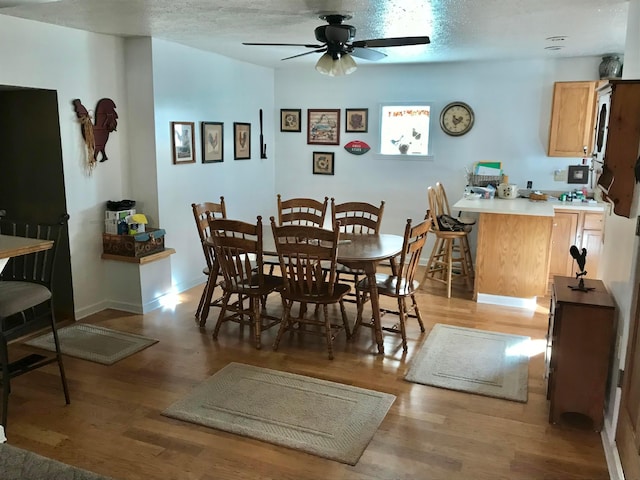 dining room featuring light wood-style flooring, a ceiling fan, baseboards, and a textured ceiling