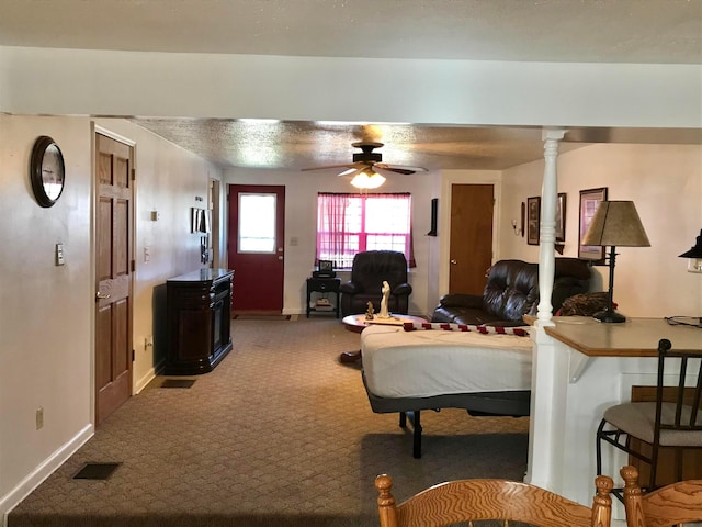 carpeted living area featuring decorative columns, baseboards, visible vents, and ceiling fan