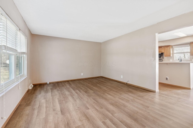 empty room with baseboards, light wood-style floors, and a sink