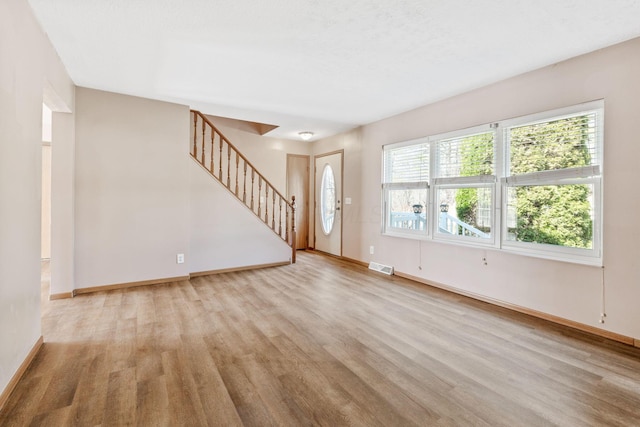 unfurnished living room with visible vents, stairway, baseboards, and wood finished floors