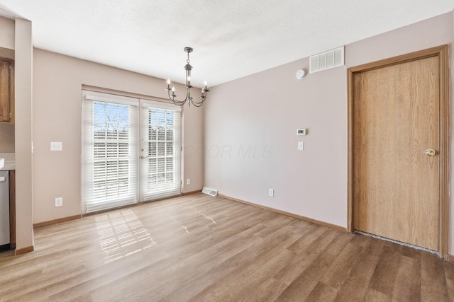 unfurnished dining area featuring a notable chandelier, visible vents, a textured ceiling, and light wood-style floors