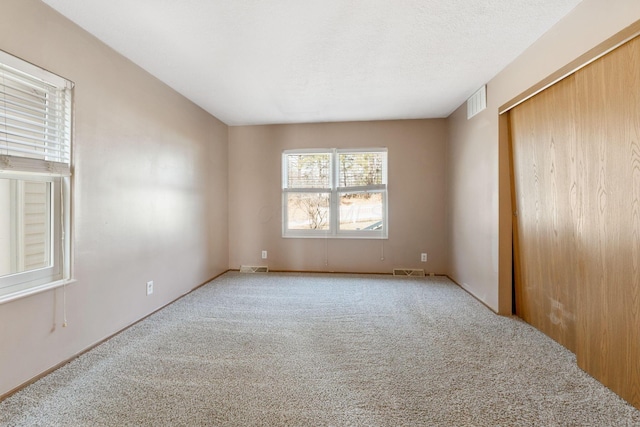 spare room featuring carpet flooring, visible vents, and a textured ceiling