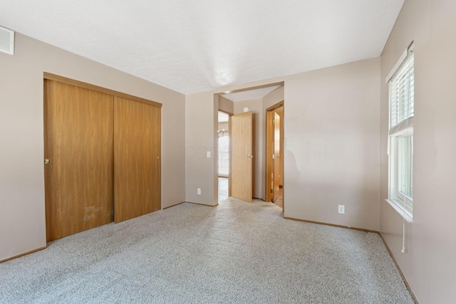 unfurnished bedroom with a closet, visible vents, light carpet, and baseboards