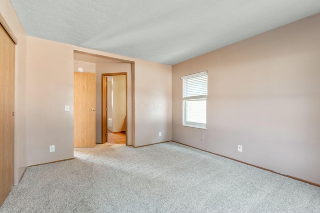 spare room with light carpet, a textured ceiling, and baseboards