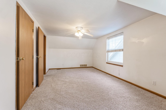 interior space featuring a ceiling fan, baseboards, visible vents, vaulted ceiling, and light carpet