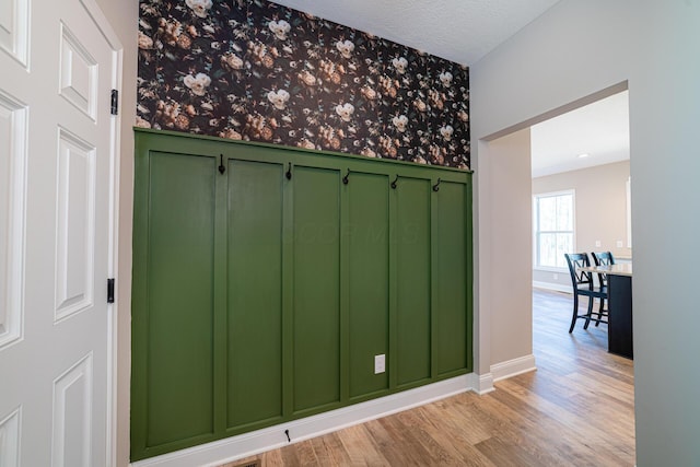 interior space with wallpapered walls, baseboards, a wainscoted wall, light wood-style flooring, and a textured ceiling