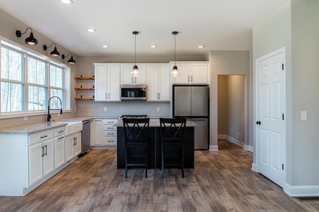 kitchen featuring open shelves, a sink, appliances with stainless steel finishes, white cabinetry, and a center island