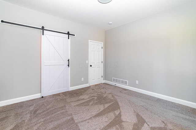 unfurnished bedroom featuring a barn door, baseboards, visible vents, and carpet floors