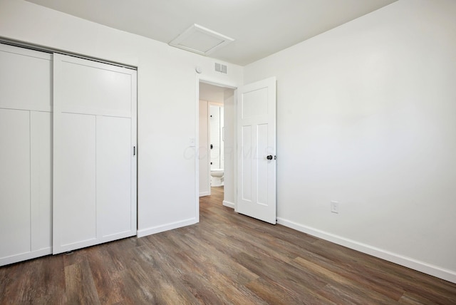 unfurnished bedroom featuring visible vents, baseboards, attic access, wood finished floors, and a closet