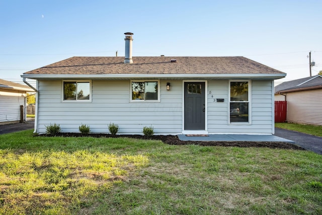 view of front facade featuring a front yard, fence, and a shingled roof