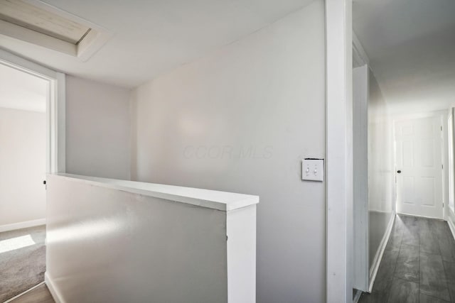 corridor featuring attic access, baseboards, and dark wood-type flooring