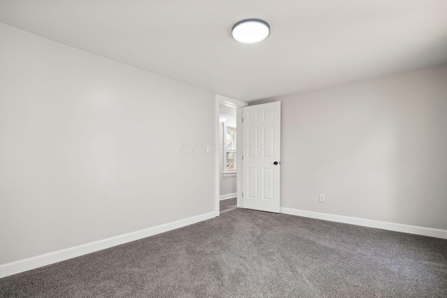 spare room with dark carpet and baseboards