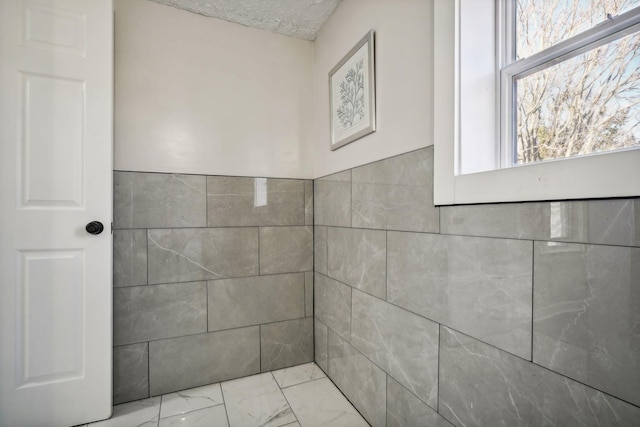 bathroom featuring marble finish floor, a textured ceiling, and tile walls