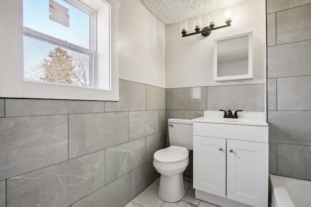 bathroom featuring toilet, vanity, a bath, marble finish floor, and a textured ceiling