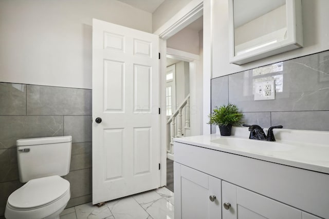 half bathroom with tile walls, marble finish floor, toilet, and vanity