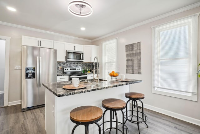 kitchen featuring wood finished floors, stainless steel appliances, a kitchen bar, crown molding, and tasteful backsplash