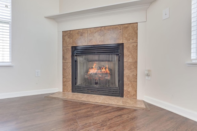 details with baseboards, wood finished floors, and a tiled fireplace