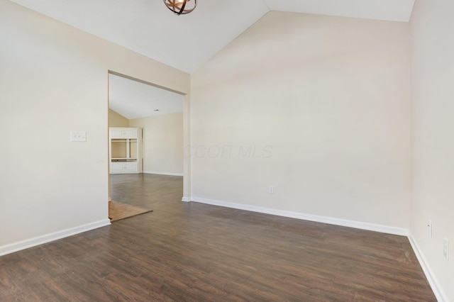 spare room with baseboards, dark wood-type flooring, and vaulted ceiling