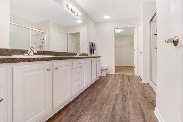 full bathroom featuring wood finished floors, double vanity, a stall shower, a sink, and a walk in closet