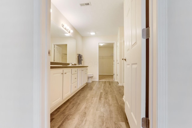 bathroom with vanity, wood finished floors, visible vents, a spacious closet, and toilet