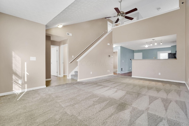 unfurnished living room featuring baseboards, carpet, stairs, a textured ceiling, and a ceiling fan