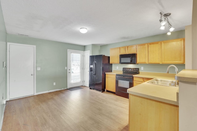 kitchen with black appliances, light wood-style flooring, light brown cabinetry, a sink, and light countertops