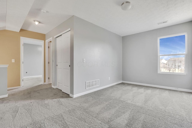 unfurnished room with visible vents, baseboards, carpet, and a textured ceiling