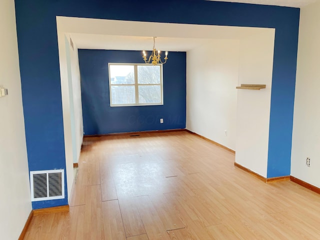 empty room featuring baseboards, wood finished floors, visible vents, and a chandelier