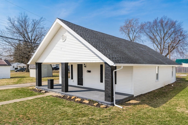 view of front of property with covered porch, roof with shingles, and a front lawn