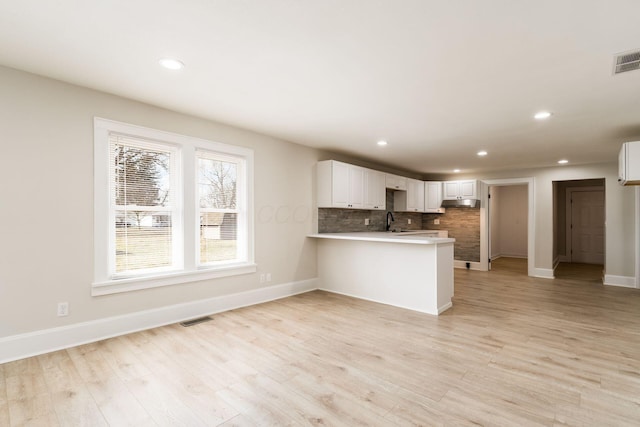 kitchen featuring tasteful backsplash, visible vents, light wood-style flooring, a peninsula, and a sink