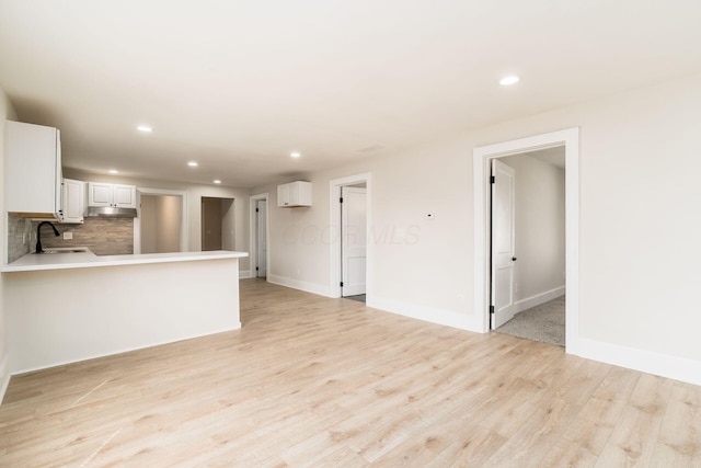 unfurnished living room featuring recessed lighting, baseboards, light wood-style floors, and a sink