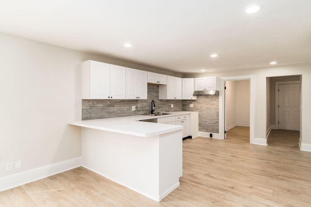 kitchen featuring white cabinets, a peninsula, light wood-style floors, and a sink