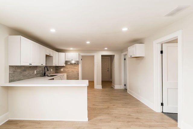 kitchen featuring visible vents, backsplash, light wood-type flooring, a peninsula, and a sink