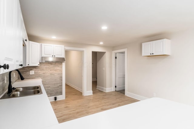 kitchen featuring under cabinet range hood, white cabinetry, light wood-type flooring, and a sink