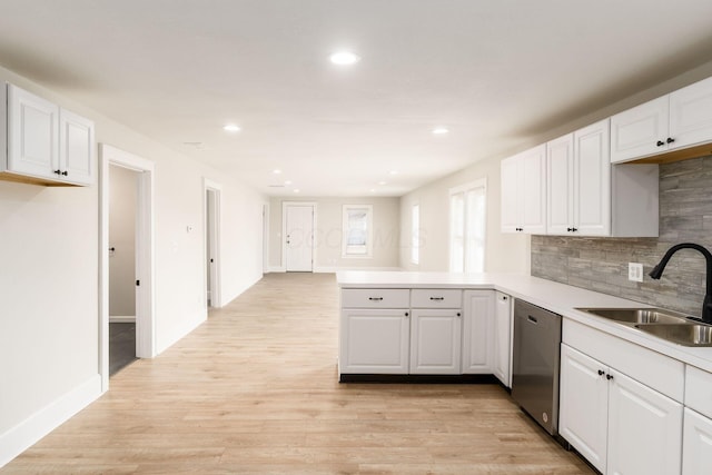 kitchen featuring a peninsula, a sink, white cabinets, light wood-style floors, and stainless steel dishwasher